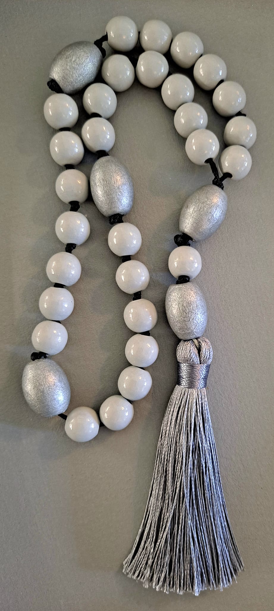 Luterilainen rukousnauha valkoisista helmistä, hopeanvärisistä välihelmistä ja hopeisesta tupsusta vaalealla taustalla.