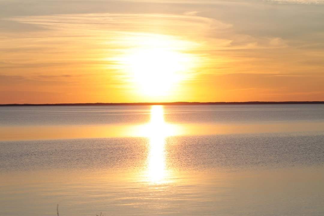 Auringonlasku järven yllä, veden pinnassa näkyy ristin muotoinen valo.