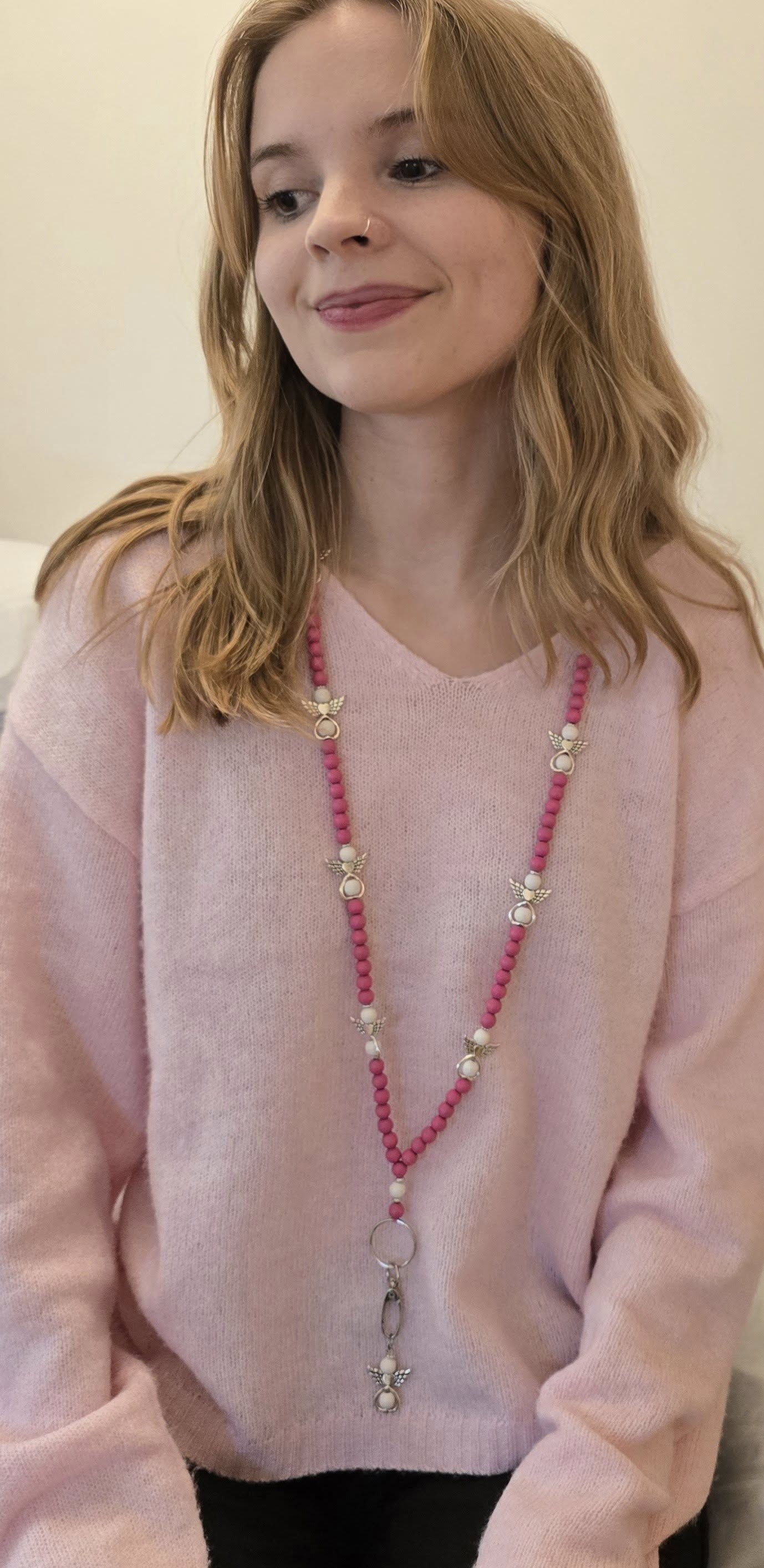 Vaaleanpunainen enkeliavainnauha puuhelmistä, avainnauha tai yli olan käytettävä malli turvalukolla, mallin kaulassa vaaleanpunaisen neuleen päällä.