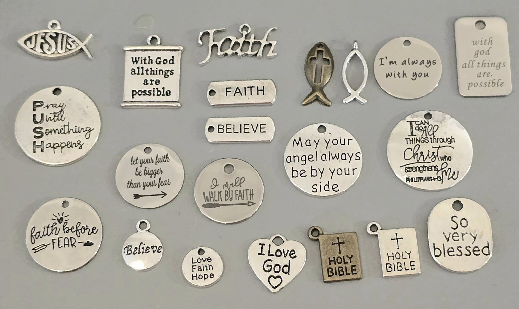 Hengelliset koruriipukset – hopeansävyisiä laattoja ja sydämiä, joissa kristillisiä tekstejä kuten Faith, Believe, I love God, Holy Bible, With God all things are possible.