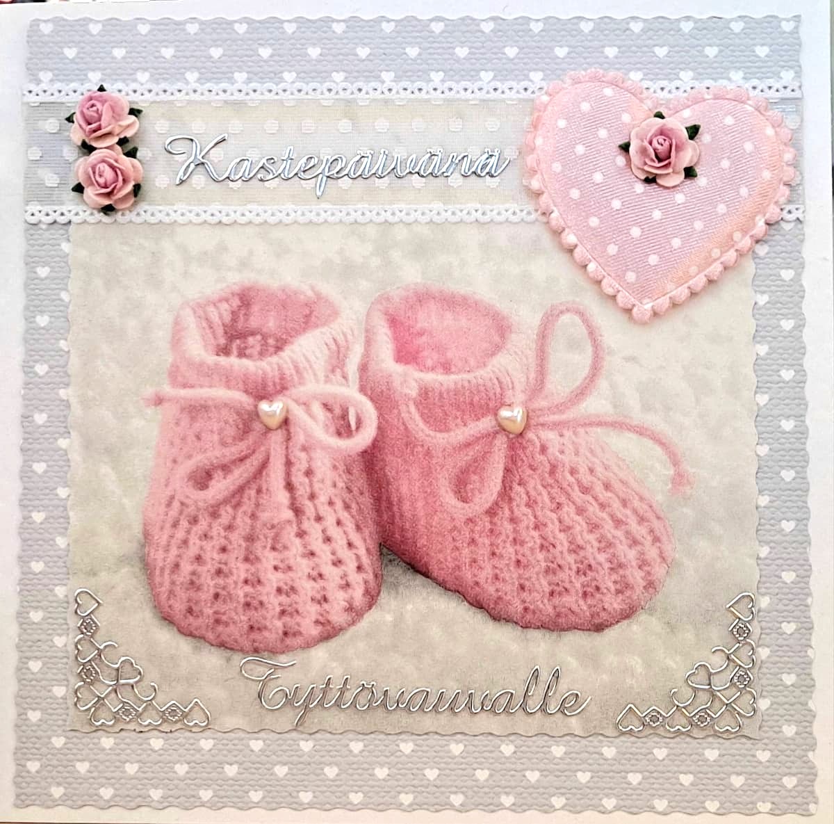 Käsintehty kastekortti tytölle, jossa on vaaleanpunaiset neulotut vauvantossut, pitsireunus ja sydänkoriste ruusulla.