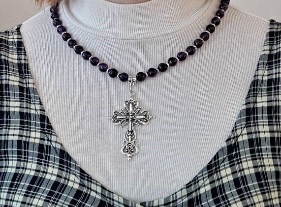 Hopeinen koristeellinen filigraaniristi kaulakorussa, jossa on violetinväriset pyöreät helmet.