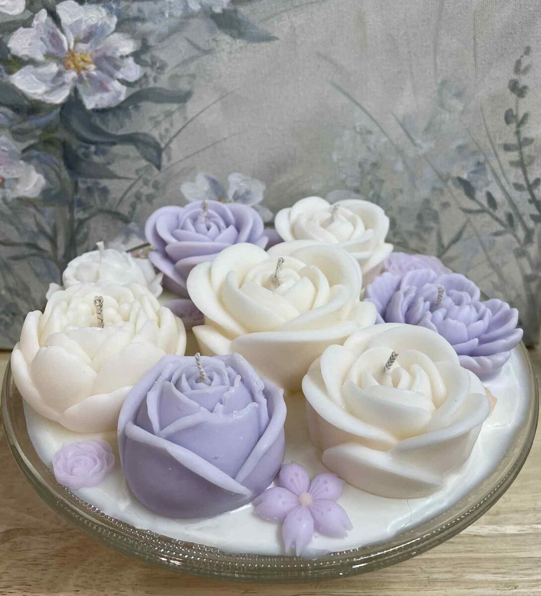 Vaaleanlilat ja valkoiset kukkakynttilät lasisessa kulhossa, taustalla kukkamaalaus.