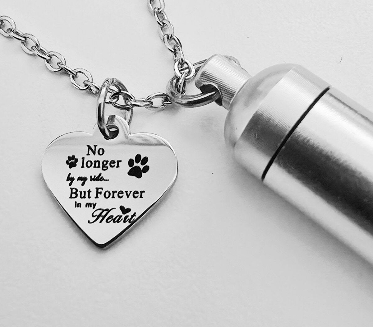 Teräksinen lemmikin muistokoru: sydänriipus tassunjäljillä ja tekstillä ”No longer by my side… But forever in my heart” sekä pieni uurna säilytystä varten.