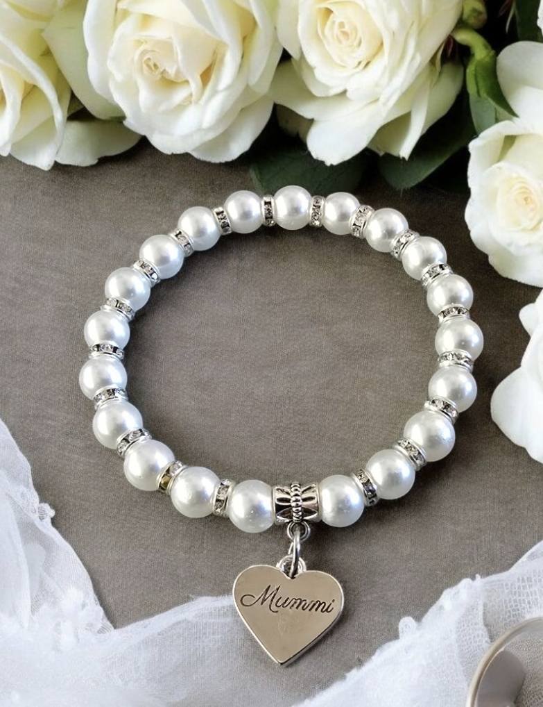 Helmirannekoru, jossa valkoiset helmet ja hopeiset välihelmet. Korussa on sydänriipus, johon on kirjoitettu sana ”Mummi”.