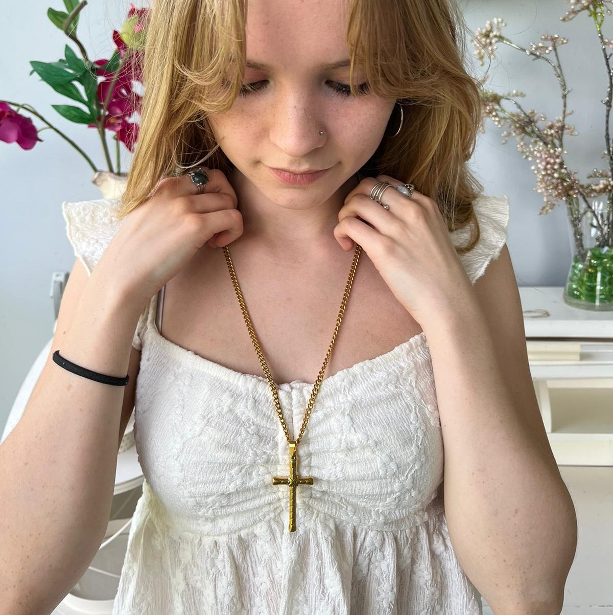 nuoren naisen kaulassa kullattu teräsristi kaulakoru valkoisen mekon päällä