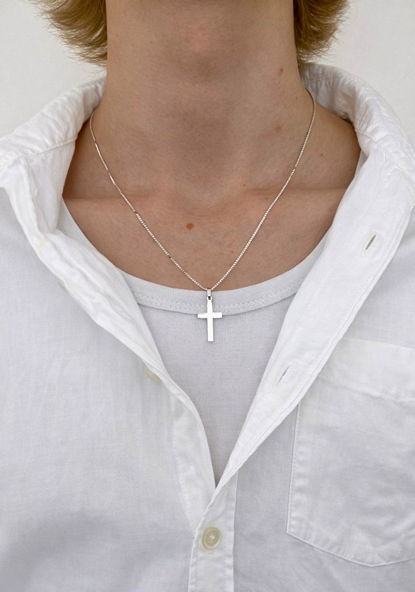 Nuoren pojan kaulassa siro hopeinen rippiristi valkoisen paidan päällä