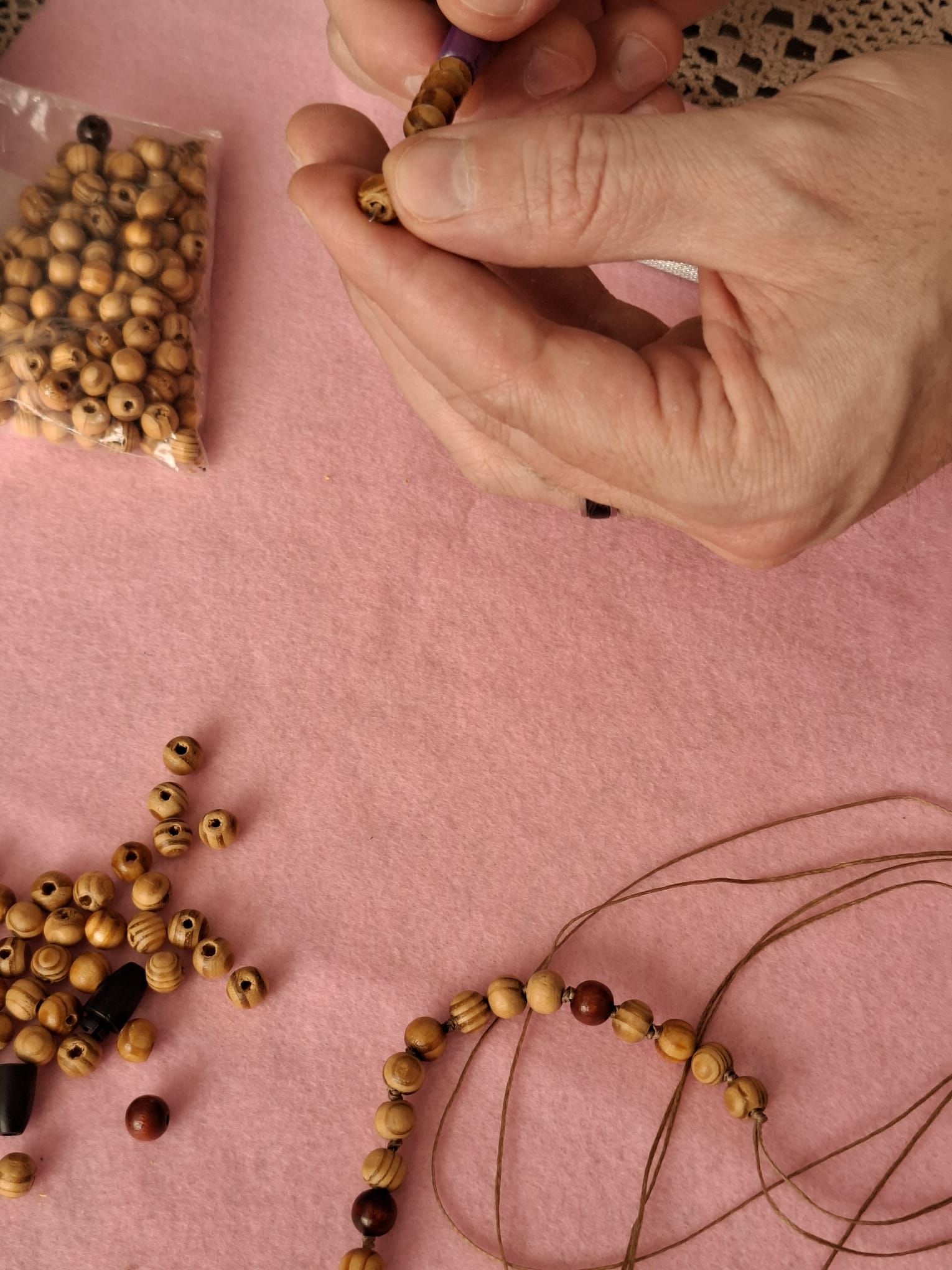 Käsin solmittava 33 helmen puuhelmirukousnauha työn alla, puuhelmet ja solmimisnauha pöydällä