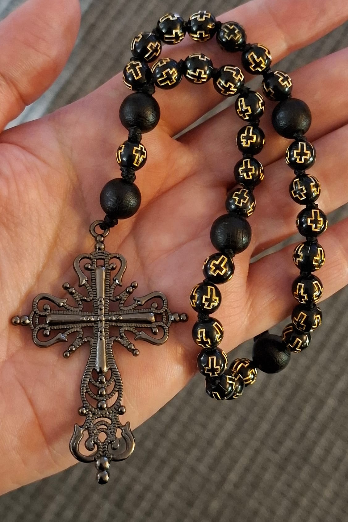 Mustista akryyliristihelmistä tehty rukousnauha jossa gunmetal sävyinen filigraaniristi avoimella kämmenellä.