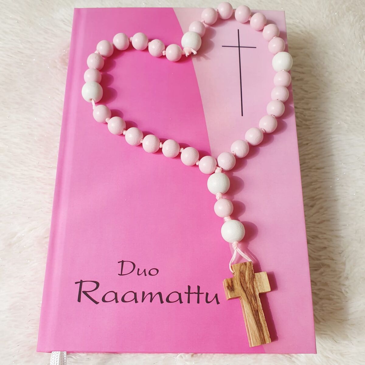 Vaaleanpunainen rukousnauha Raamatun päällä sydämen muotoon aseteltuna, oliivipuuristi Israelista rukousnauhan päässä, vaaleanpunainen Raamattu alla.